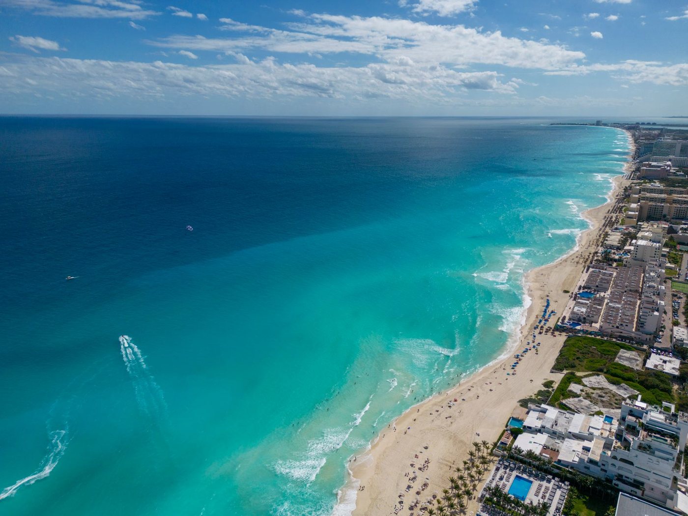 Aerial view along a resort beachfront, hotels and pools on the shoreline beside the sea