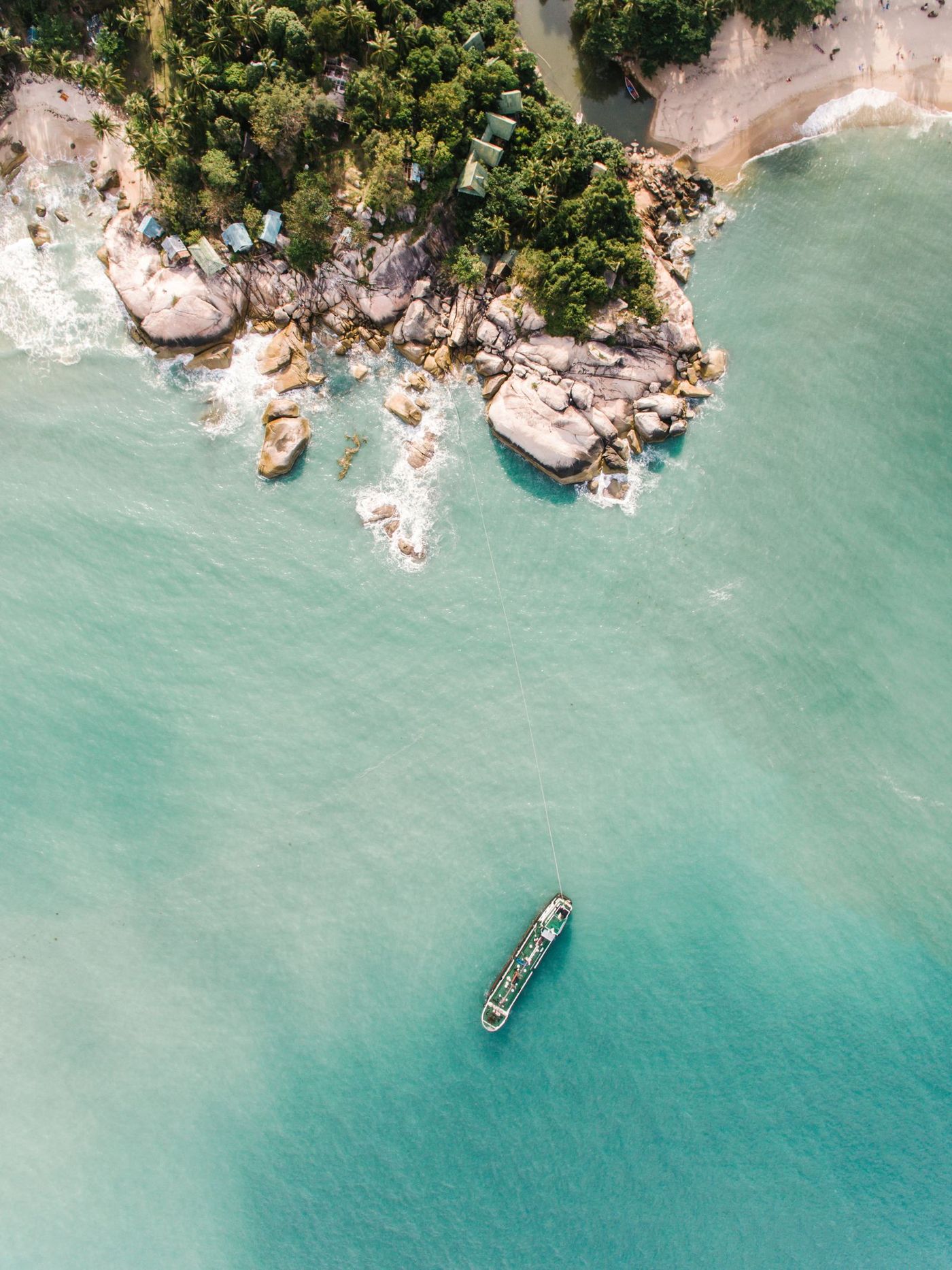 Aerial view straight down on a rocky headland with a boat moored offshore